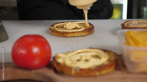 The chef puts white sauce on half a grilled burger bun, demonstrating the cooking process of mouth-watering burgers in the restaurant kitchen.