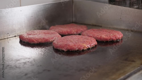 Close-up of four hamburger patties being fried on a hot industrial stove in a restaurant kitchen. The process of making juicy, mouth-watering burgers is fast food.