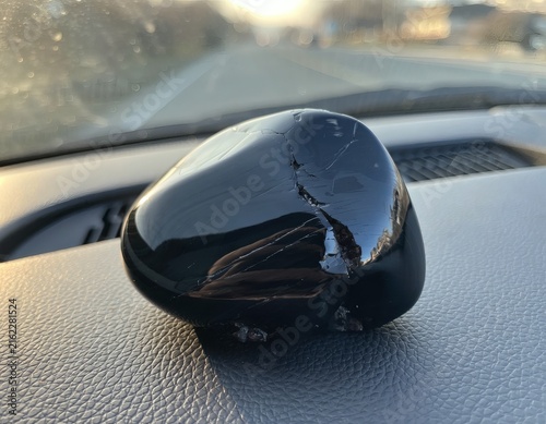 Smooth Obsidian Stone on Car Dashboard Reflecting Windshield View as Travel Talisman