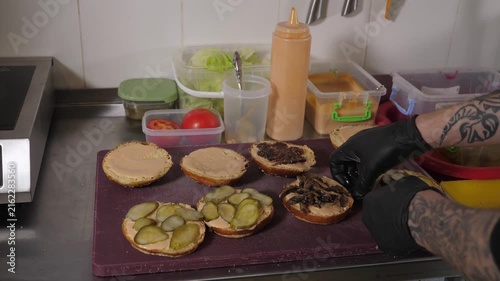 A close-up of the chef preparing four burgers in the kitchen of a fast food restaurant, where he spreads the buns with sauce. Unhealthy food.