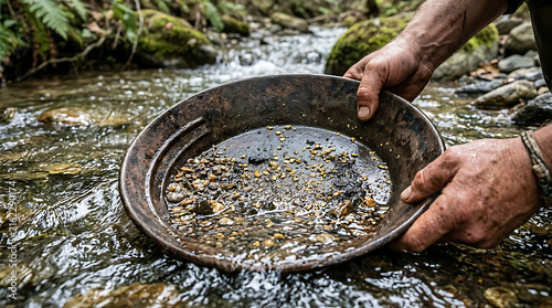 Hands holding a metal pan with gold flakes in a stream.