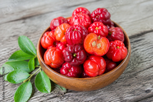 Fresh acerola cherries in wooden bowl with leaves on grey table, healthy fruit and natural food concept