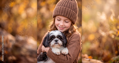 Happy little girl hugging her cute shih tzu dog in autumn park. Warm golden hour portrait of child and pet friendship.