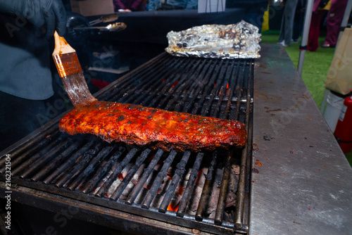 Cuadro en lienzo A close-up shot of a chef basting savory glazed pork ribs on a hot metal barbecue grill outdoors during a catering event