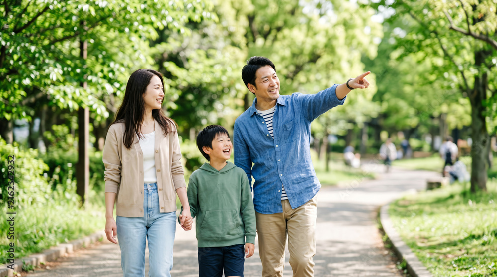 Fototapeta premium 新緑の公園を笑顔で散歩しながら遠くを指差す仲良し家族