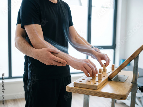 Therapist assisting patient with hand movement exercise on pegboard during physical rehabilitation session.