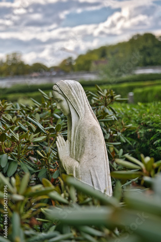 Betende Marienfigur inmitten  von grünem Rhododendron auf dem Hauptfriedhof Mülheim Ruhr