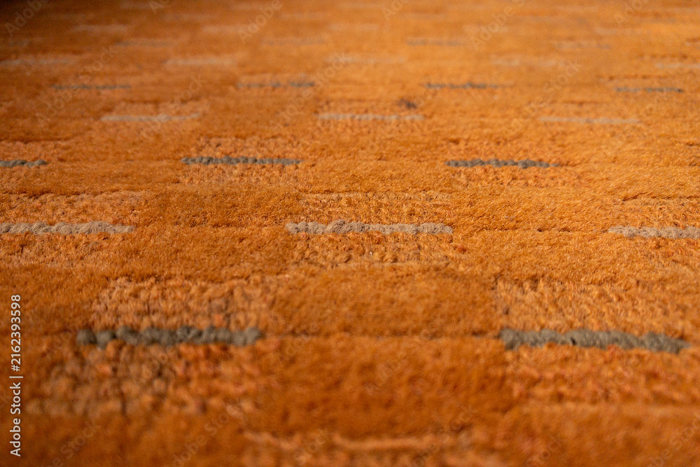 Fototapeta premium Close-up view of an orange textured carpet with subtle gray stripes and plush fibers, ideal as an interior design background conveying warmth, comfort and a cozy modern home atmosphere.