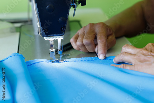 Hands guiding blue fabric through a sewing machine, highlighting tailoring, garment production, textile manufacturing, craftsmanship, precision, and fashion industry, close-up