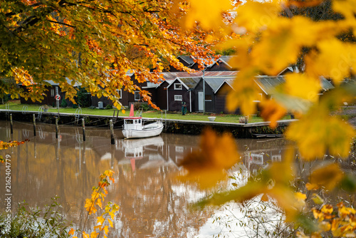 Small boat floating on a calm river surrounded by colorful autumn trees in Skåne, Sweden. Peaceful seasonal landscape, creating a scenic atmosphere for outdoor recreation and travel.
