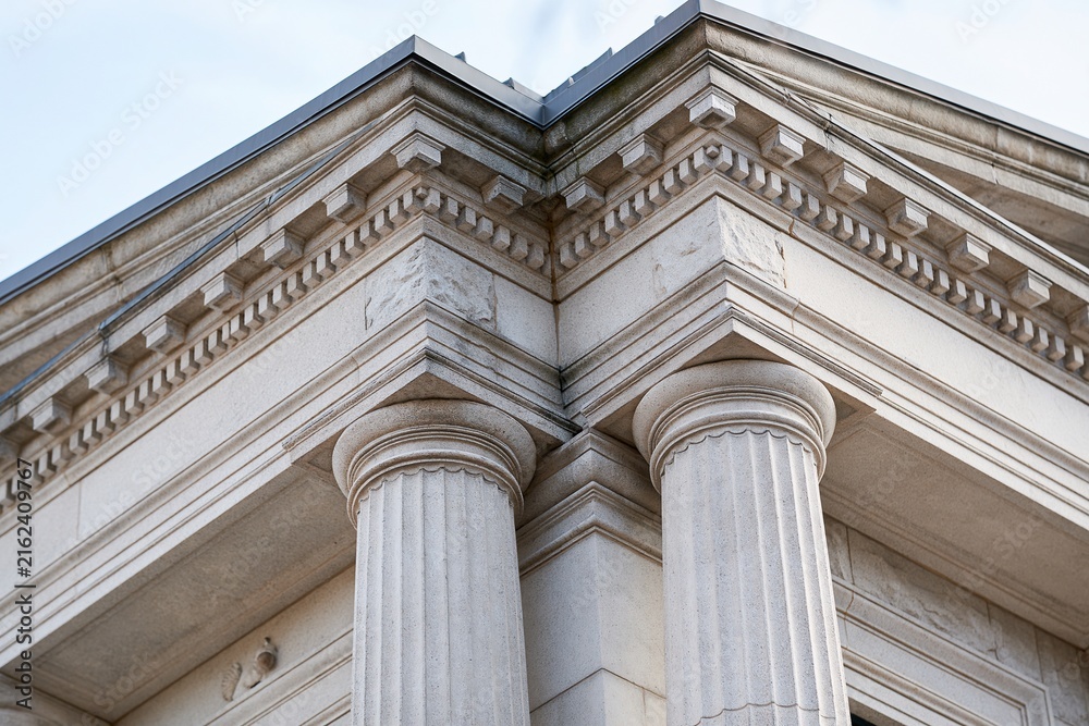 Naklejka premium Detailed Close-up of Classical Architectural Columns and Cornice Against a Bright Sky