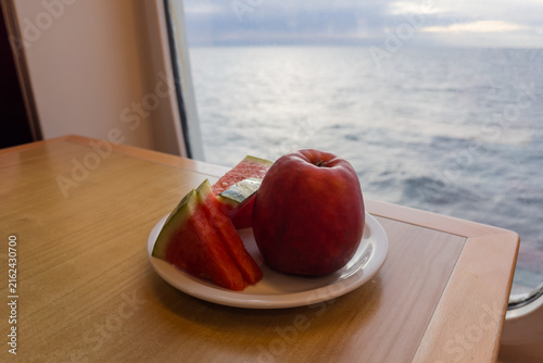 Quadro su tela Watermelon slices and red apple on plate against sea view