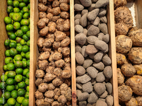 Fresh Traditional Spices and Roots Market Display. Vibrant wooden trays featuring fresh kaffir limes, ginger roots, kluwek nuts, and aromatic tubers at a local spice bazaar.