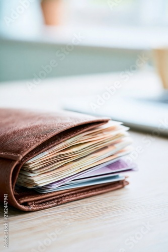Richly Detailed Brown Leather Wallet Filled with Assorted Banknotes and Cards on a Wooden Surface