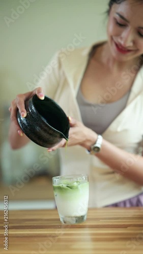 Young Woman Pouring Matcha Green Tea into Iced Latte Glass at Home Kitchen Counter