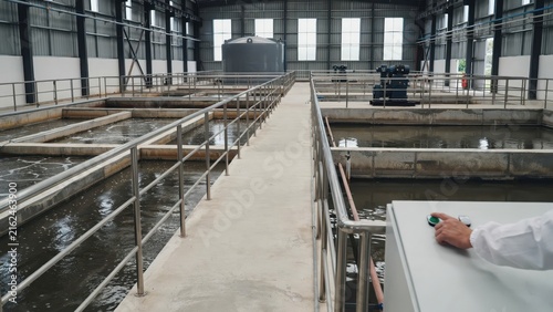 Industrial wastewater treatment plant interior with aeration tanks. This facility shows an engineer operating water purification equipment for environmental sustainability.