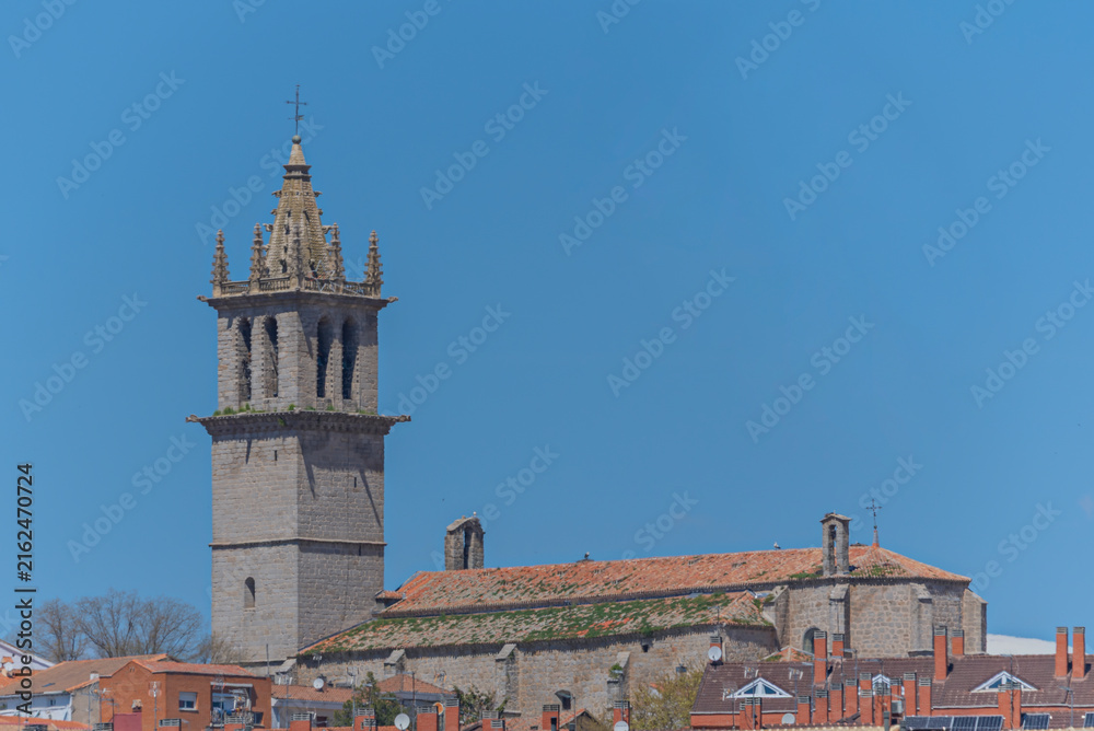 Obraz premium Historic Spanish stone church with Gothic bell tower and moss-covered tiled roof overlooking town rooftops.