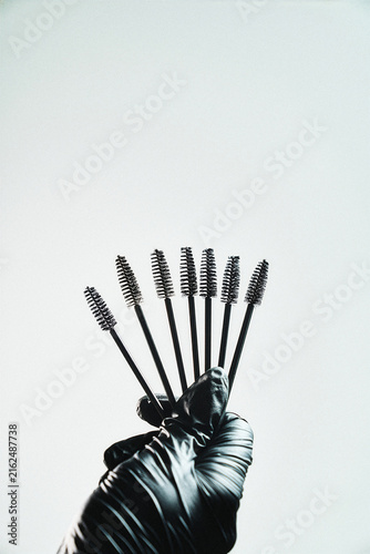Fan of black mascara wands held by a gloved hand