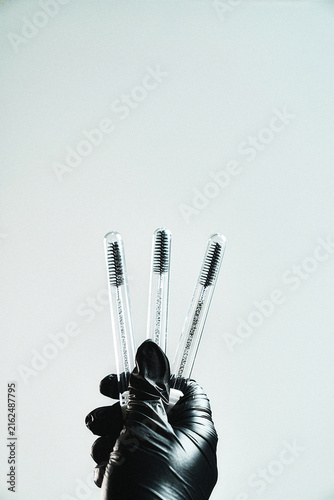 Hand holding three disposable mascara wands on light grey background