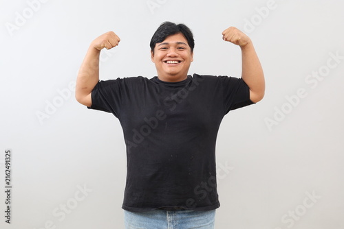 Canvastavla A stout, strong, and jovial man is showing off his strength by raising his arm and clenching his fist to display his muscles, smiling as he stands in front of a white wall