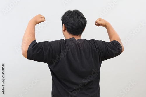 Obraz na plátne A rear view of a burly, heavy-set man showing off his strength by raising his arms and clenching his fists to display his muscles, standing in front of a white wall