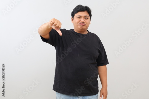 Obraz na plátne A heavy-set man appearing dissatisfied, annoyed, disappointed, and sad gives a thumbs-down gesture to signal disapproval, set against a white background
