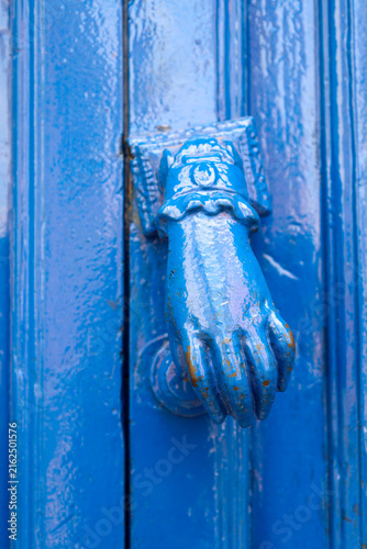 Fotografie Blue painted doorknocker with hand shape on blue wooden door