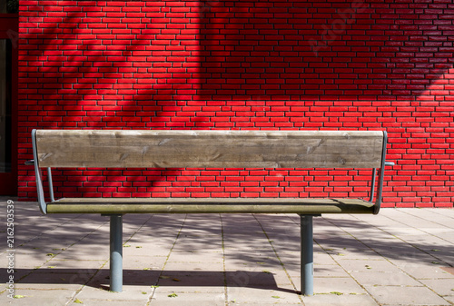 Empty wooden bench with red tile wall in the background.