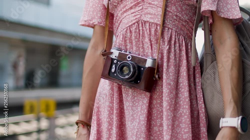 The girl in a pink dress and with a camera is standing on the platform of the train station. film camera. travel and vacation. creating content about travels.
