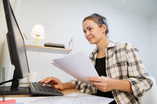 Фотография Working with paper documents and computer at a home desk, comparing information, checking records and completing business paperwork