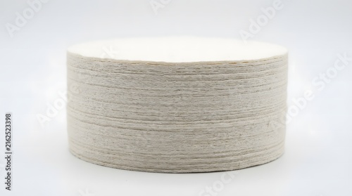 Stack of circular beige paper coffee filters with textured edges on white surface.