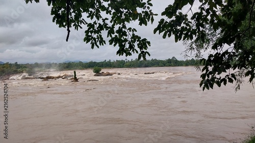 Canvastavla A serene view of a turbulent river surrounded by lush greenery and overcast skies