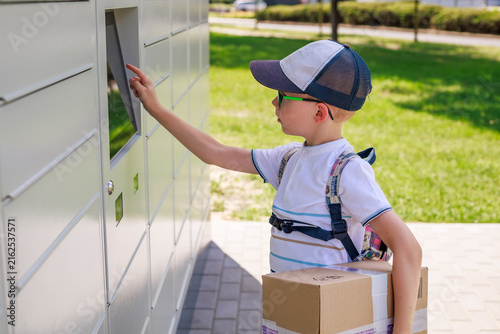 Foto Young boy holding a cardboard package while using the touchscreen of an automated parcel locker