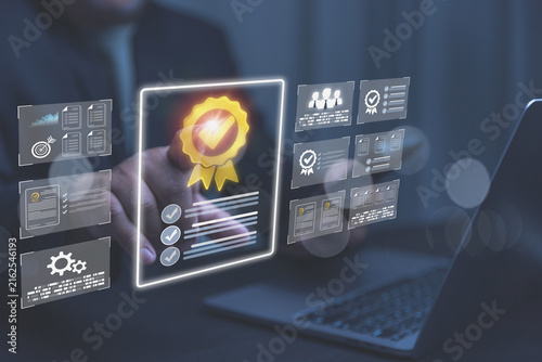 A businessman uses a laptop while interacting with a glowing digital quality certification. Multiple holographic screens show standard compliance checklists and team data graphics.