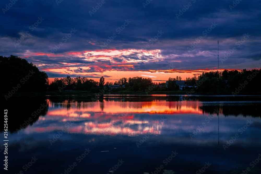 Obraz premium Dramatic dark blue twilight sky with glowing orange sunset slit reflected on lake
