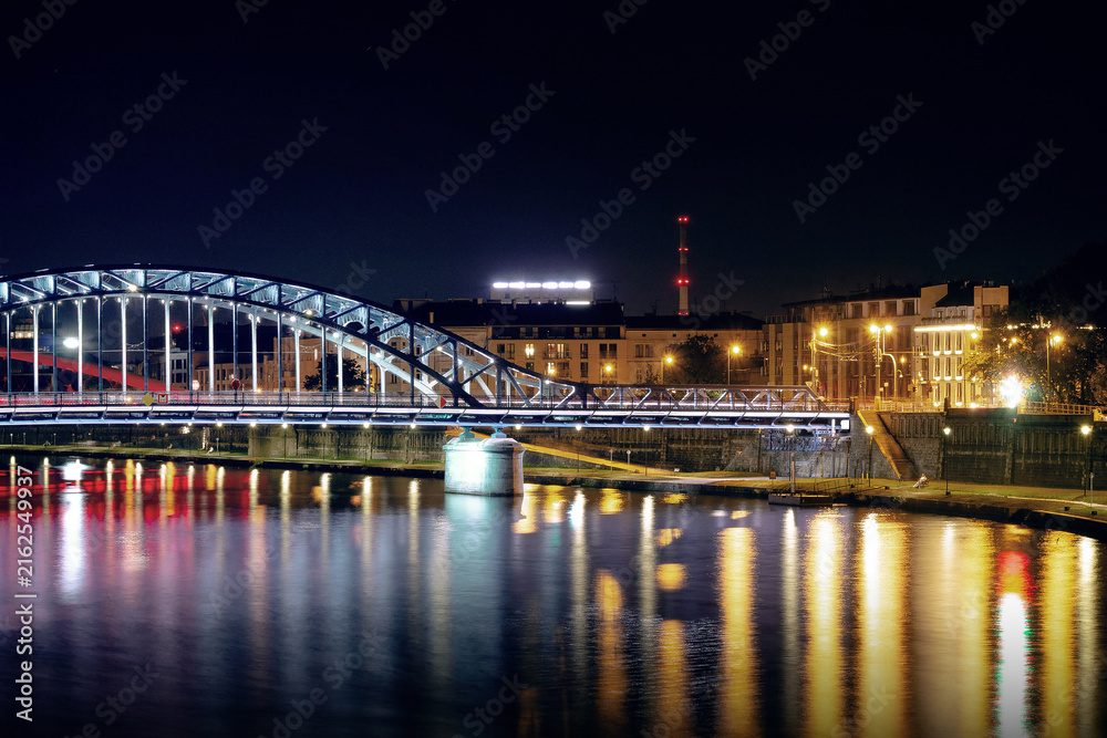 Fototapeta premium Horizontal night riverside photo of Jozef Pilsudski bridge lights reflected on water real life photography