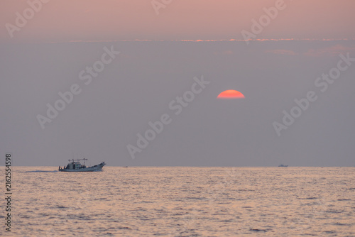 Photography Bateau de pêche naviguant sous un soleil couchant rouge à l’horizon marin
