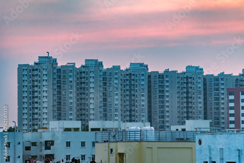 Fotografie Bengaluru cityscape at sunset, showcasing numerous apartment buildings under a soft pink sky
