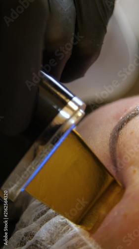 Professional beautician applying cleansing mask on female client's face. Close-up of female face during youth restoration and facial rejuvenation procedure  - Vertical Video