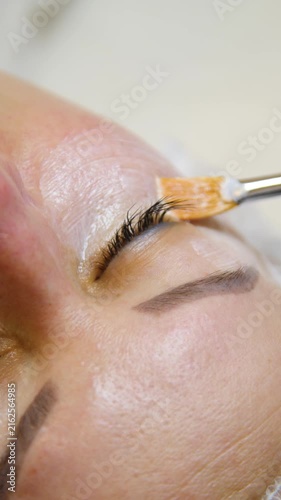 Professional beautician applying cleansing mask on female client's face. Close-up of female face during youth restoration and facial rejuvenation procedure  - Vertical Video