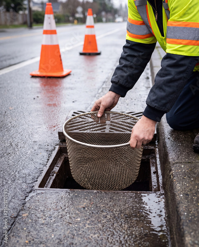 Worker installing a mesh trash trap in a storm drain grate