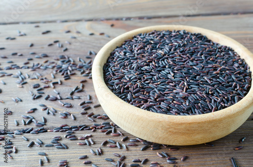 Bild auf Leinwand Organic Black Rice in a ceramic bowl with grains scattered around on a wooden table