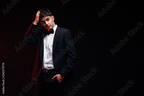 Handsome young man in black tuxedo touching face with copy space