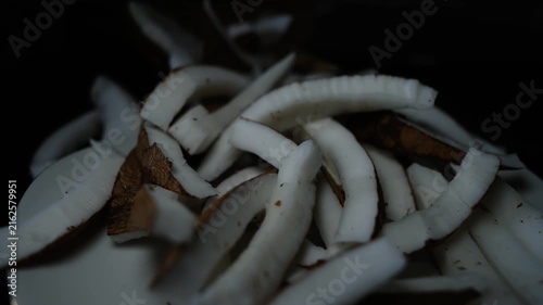 Close up of sliced coconut pieces with white flesh and brown shell on a dark background