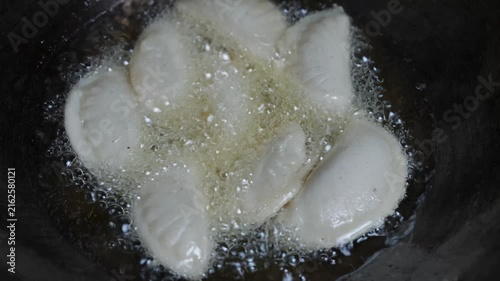 Dumplings frying in hot oil in a dark pan, with bubbling oil and close-up view of homemade food cooking