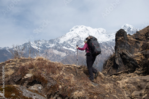 Eine Frau mit großem Rucksack steigt einen Bergpfad empor und erblickt das Bergpanorama der Annapurna Bergkette im Himalaya