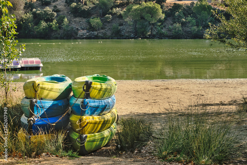 Stacked pedal boats beside a green lake at La Depuradora recreation area in Pelayos de la Presa, Madrid, Spain.