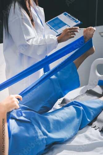 Doctor checks Asian senior woman patient after knee replacement operation in hospital room. Nurse examines leg after surgery. Medicine health treatment therapy healthcare concept