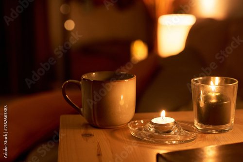 Fotografie Ceramic mug and burning candles sitting on wooden table in dimly lit room, representing relaxation and self care