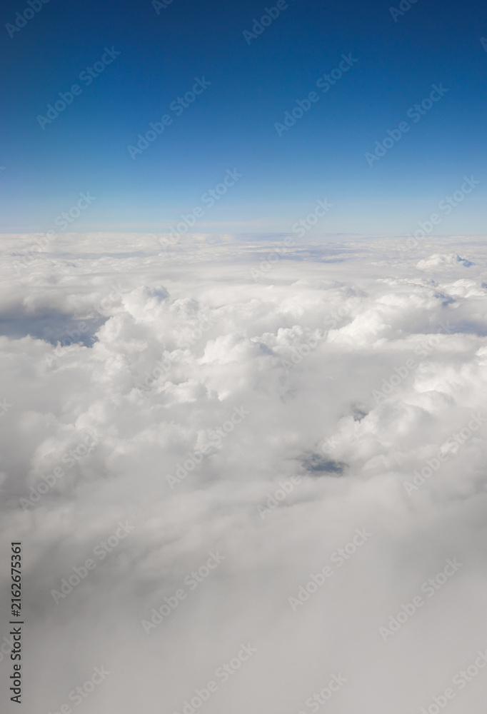 Fototapeta premium Clouds floating high in the clear blue sky, creating a serene and vast atmospheric view from an airplane window